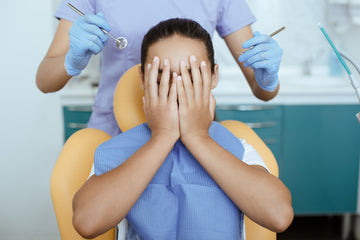 Patient covering face in fear at dentist appointment, representing dental anxiety